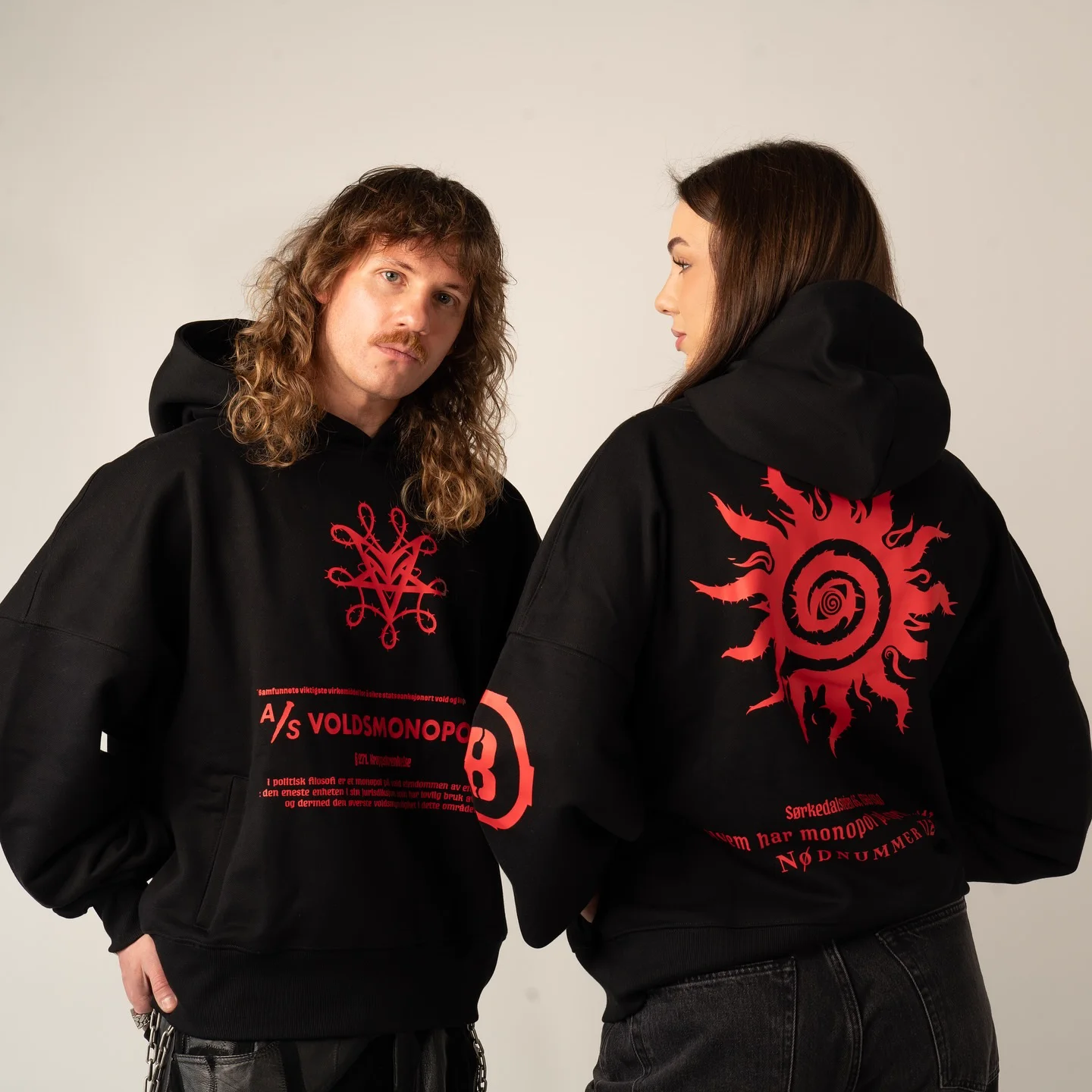 Two models in the Voldsmonopol hoodie, the front sigil and A/S VOLDSMONOPOL on one, the red sun across the back of the other